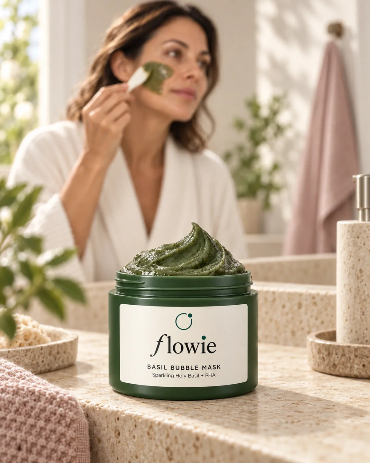 Basil Bubble Mask jar in a warm bathroom setting with a woman in a cream robe